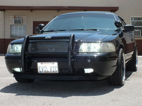 2003 Ford Crown Victoria - Low front shot of murdered-out Crown Vic, brush guard, headlights lit, EVIL VIC plate.