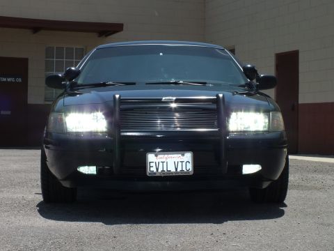 2003 Ford Crown Victoria - Head-on view of blacked-out Crown Vic, brush guard, headlights on, EVIL VIC plate.