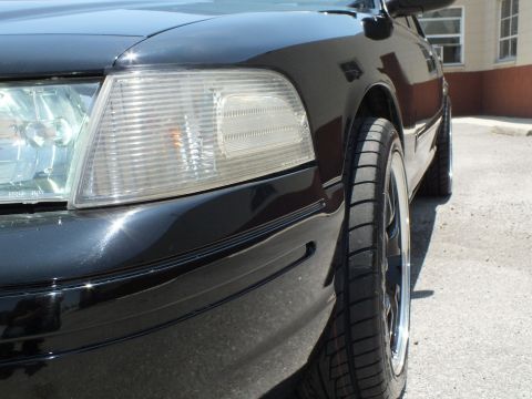 2003 Ford Crown Victoria - Detail of clear front corner lamp and black fender with chrome-lip wheel behind.