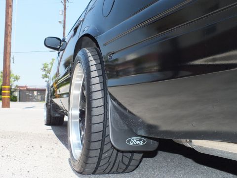 2003 Ford Crown Victoria - Low-angle view of a lowered black Ford sedan's rear tire, polished-lip wheel and Ford-logo mud flap.