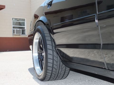 2003 Ford Crown Victoria - Close low view of a black sedan's front wheel and fender, polished-lip wheel against a brick wall.