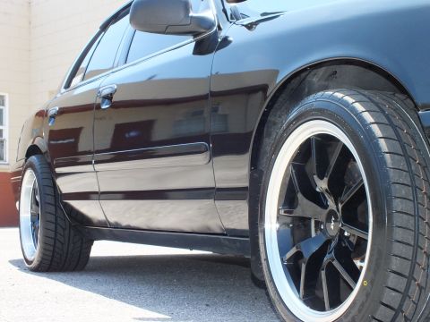 2003 Ford Crown Victoria - Side view of a black Ford sedan's front door and wheel with a black machined-lip wheel.