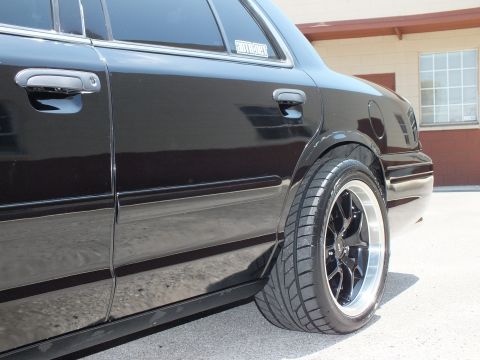 2003 Ford Crown Victoria - Side angle of a black Ford sedan's rear door and wheel with a black machined-lip wheel.