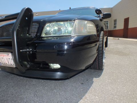 2003 Ford Crown Victoria - Low close view of a black Ford sedan's front corner showing grille guard, spotlight and headlight.