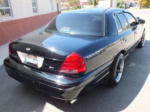 2003 Ford Crown Victoria - Rear three-quarter of a lowered black Ford sedan showing SVT badge, dual exhaust and polished-lip wheels.