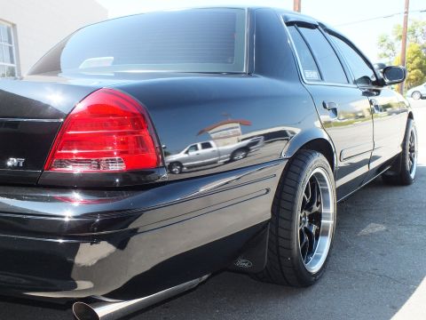 2003 Ford Crown Victoria - Sunlit rear quarter of a black Ford sedan showing SVT badge, polished-lip wheel and Ford mud flap.