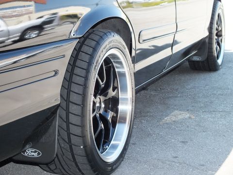 2003 Ford Crown Victoria - Side profile of a lowered black Ford sedan riding on black machined-lip wheels with Ford mud flaps.