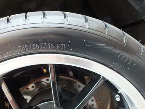 2003 Ford Crown Victoria - Close detail of a tire sidewall marked 285/35 ZR18 97W above a cross-drilled brake rotor.