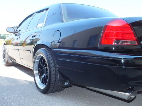 2003 Ford Crown Victoria - Rear quarter of a black Ford sedan showing the taillight, black wheel, Ford mud flap and exhaust tip.