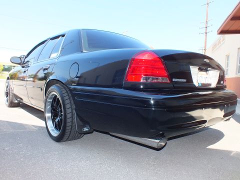 2003 Ford Crown Victoria - Rear three-quarter of a lowered black Ford sedan with Ford trunk badge, dual exhaust and black wheels.