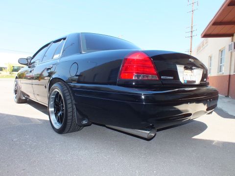 2003 Ford Crown Victoria - Rear three-quarter of a black Ford sedan with Ford emblem, dual exhaust and black polished-lip wheels.