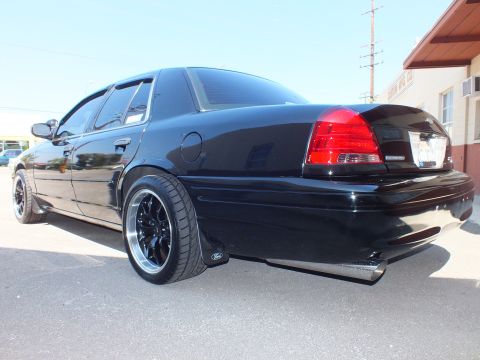 2003 Ford Crown Victoria - Lowered black Crown Victoria sedan parked in a lot, showing tinted glass, black aftermarket wheels and Ford mud flap.