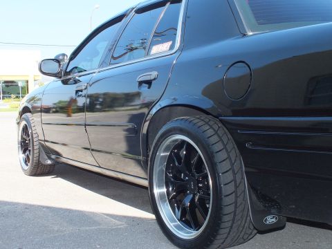 2003 Ford Crown Victoria - Close rear-quarter shot of a black Crown Victoria fuel door, fender and black machined-lip wheel.