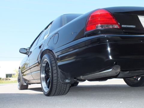 2003 Ford Crown Victoria - Low rear-quarter of a black Police Interceptor showing red taillight, black wheel and chrome exhaust tip.
