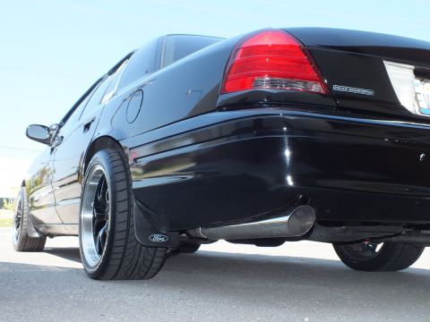 2003 Ford Crown Victoria - Ground-level black Police Interceptor rear quarter, Ford mud flap and twin exhaust tips beneath the bumper.