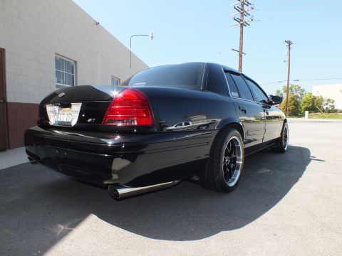 2003 Ford Crown Victoria - Black Crown Victoria parked by a wall, rear three-quarter showing low stance and chrome side-exit exhaust.