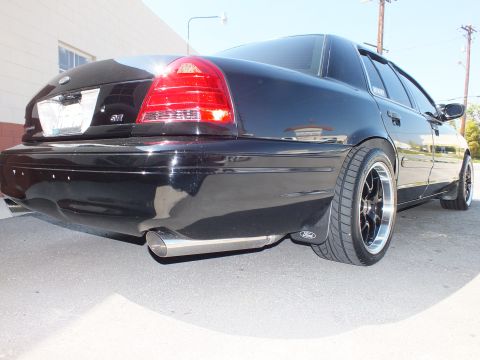 2003 Ford Crown Victoria - Low rear three-quarter of a black Crown Victoria near a building, chrome exhaust tip and black wheels visible.