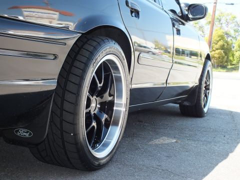 2003 Ford Crown Victoria - Low close-up of a black Crown Victoria front wheel and fender, Ford mud flap behind the tire.