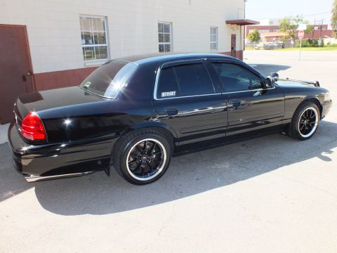 2003 Ford Crown Victoria - Side profile of a black Crown Victoria sedan beside a building, riding low on black machined-lip wheels.