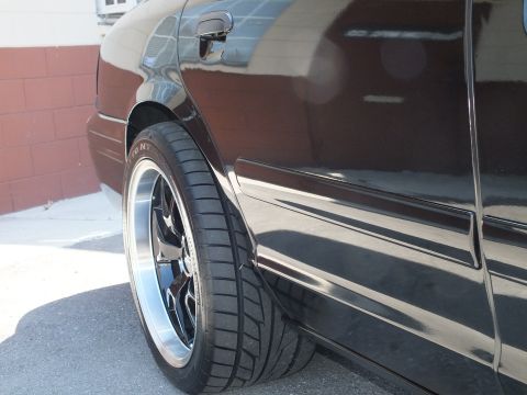 2003 Ford Crown Victoria - Low close-up of a black Crown Victoria rear wheel and fender, glossy paint reflecting a nearby wall.
