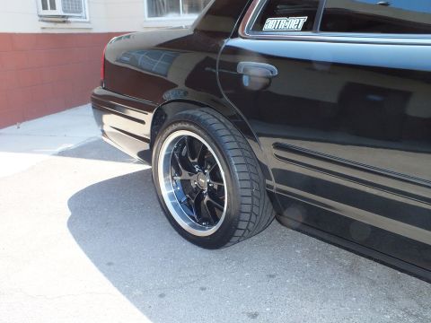 2003 Ford Crown Victoria - Black Crown Victoria rear wheel close-up with machined-lip wheel and a window decal on the glass above.
