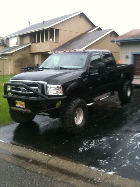 1990 Chevrolet Suburban - A black Ford F-Series truck with oversized tires is parked in front of a suburban house.