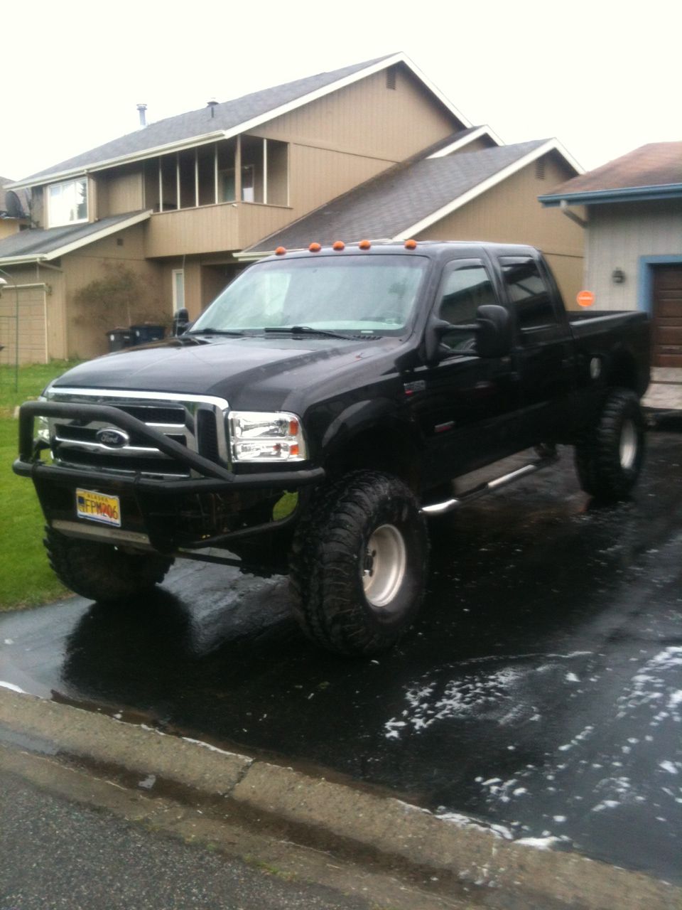 Black Ford F-Series truck with aftermarket bumper and large tires parked on wet asphalt