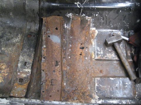 1973 Ford Ranchero - Extensive rust damage to the floor pan of a vehicle, with a hammer resting on the corroded metal.