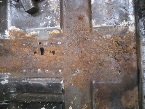 1973 Ford Ranchero - Close-up view of a heavily rusted vehicle floor pan, showing significant corrosion and debris. The image includes visible spot welds.