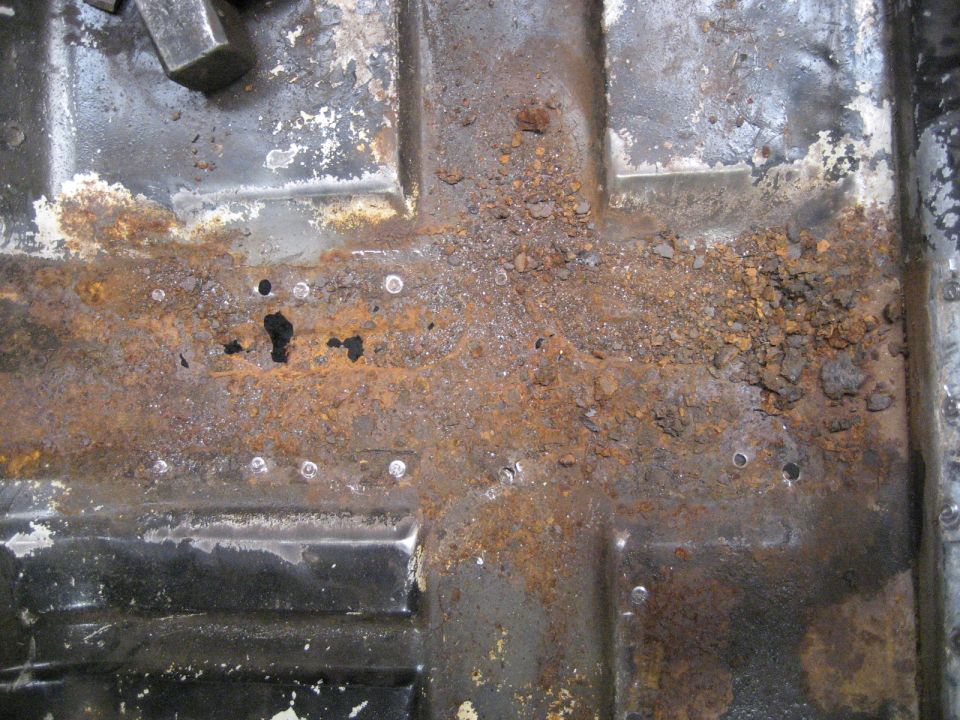 Rusted floor pan with debris and visible spot welds