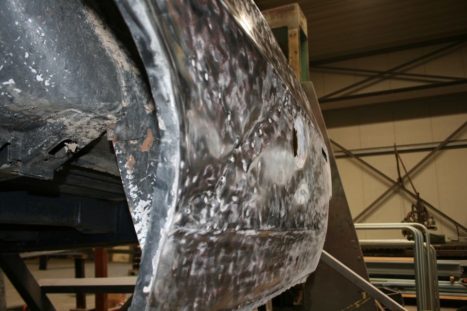 Car body panel with rust and dents, showing metal preparation for repair