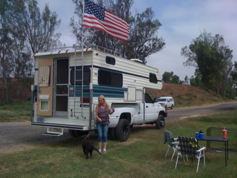 1968 Ford Mustang - A woman and her dog stand next to a white camper truck flying an American flag.