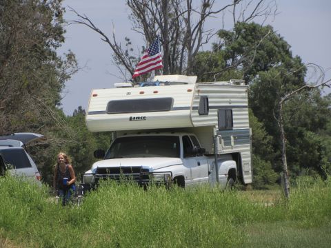 1968 Ford Mustang - A pickup truck camper setup flies an American flag, with another vehicle nearby in a grassy field.