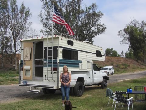 1968 Ford Mustang - A woman and her dog are parked next to a camper truck, with another vehicle visible in the background.