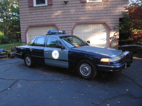 2001 Ford Crown Victoria - A two-tone police car sits in a driveway in front of a house with a double garage door.