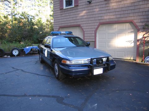 2001 Ford Crown Victoria - A blue police car, identified as a 2001 Ford Crown Victoria, is parked in front of a garage.