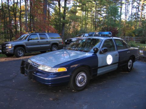 2001 Ford Crown Victoria - A police car and an SUV are parked in a driveway with trees in the background.