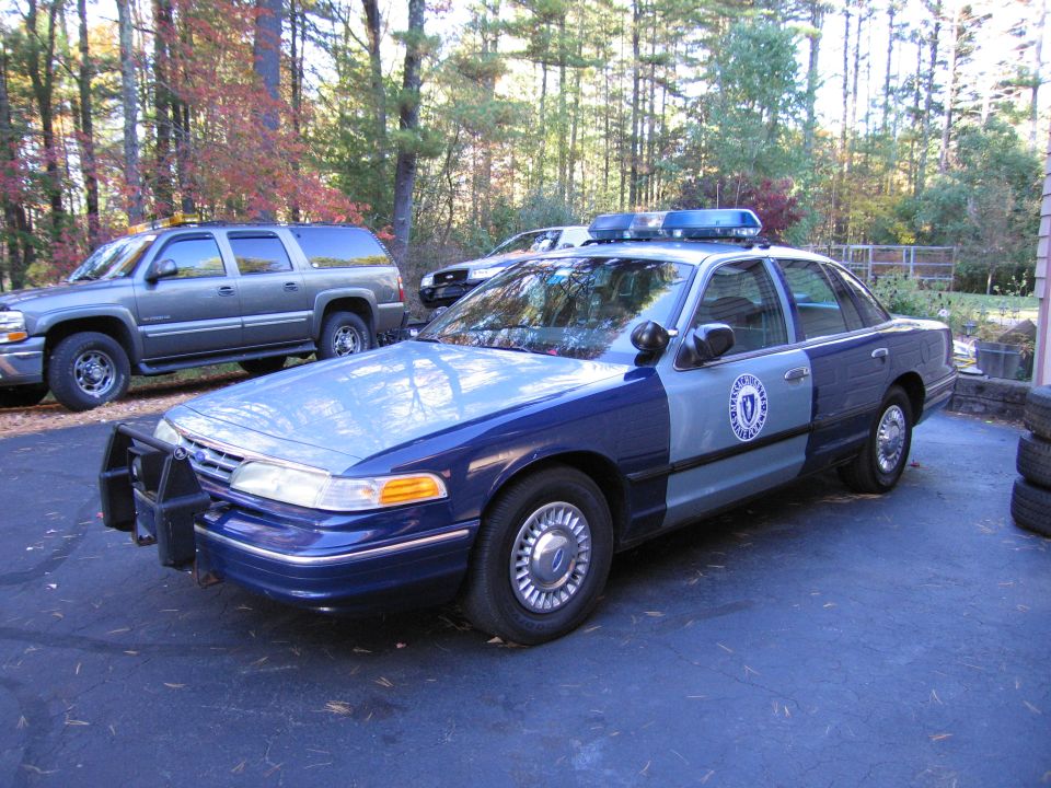 Blue and gray police car with a push bumper and light bar, parked on asphalt