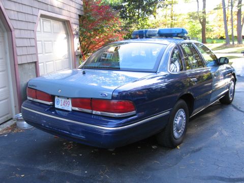 2001 Ford Crown Victoria - A blue and grey police car is parked in a driveway, with a garage and trees in the background.