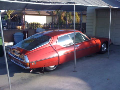 1968 Ford Mustang - A red Citroën SM is parked in a driveway under a carport, showing its distinctive fastback design.