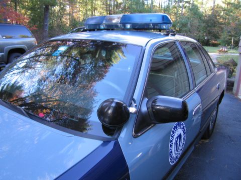 2001 Ford Crown Victoria - Massachusetts police car, likely a 2001 Ford Crown Victoria, parked outdoors with trees reflected in the windshield.