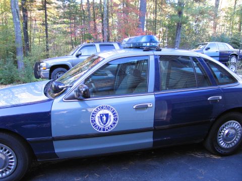 2001 Ford Crown Victoria - A Massachusetts State Police Ford Crown Victoria is seen parked next to another vehicle, with trees in the background.