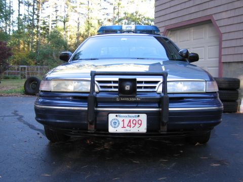 2001 Ford Crown Victoria - A blue 2001 Ford Crown Victoria police car is parked in front of a garage, a push bumper and emergency light bar.