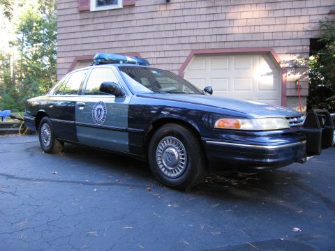 2001 Ford Crown Victoria - Police car with light bar on roof and push bumper parked in front of a garage.