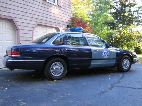 2001 Ford Crown Victoria - Side view of a dark blue and light blue police car, likely a 2001 Ford Crown Victoria, parked on asphalt.