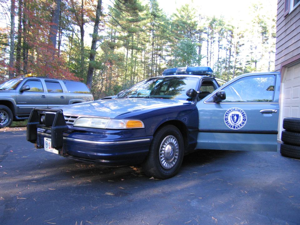 Massachusetts State Police Crown Victoria parked next to a garage, with an SUV in the background