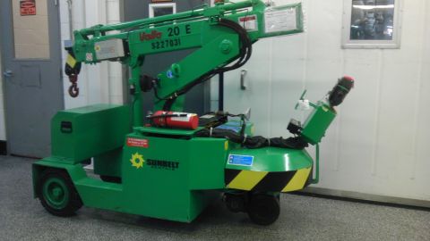 1989 Ford Bronco - A green industrial crane is parked indoors, a hook and safety markings.