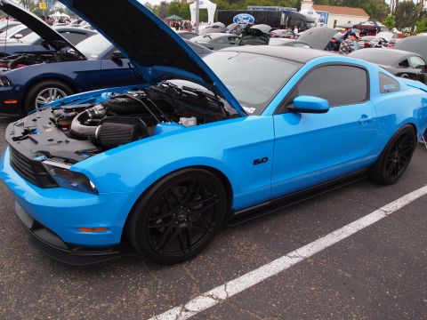 1994 Ford Bronco - A bright blue Ford Mustang with its hood open, revealing the engine, is parked at an outdoor event.