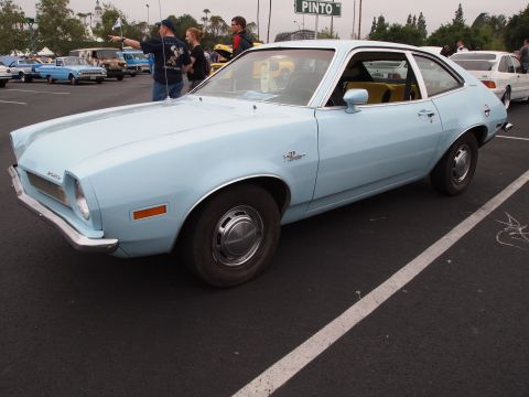 1994 Ford Bronco - A light blue Ford Pinto is parked in a lot with other vehicles and people around.