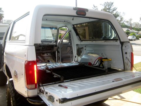 1996 Ford Bronco - Interior of a white SUV is visible with the tailgate down, and the word 'Outback' is seen on the windshield.